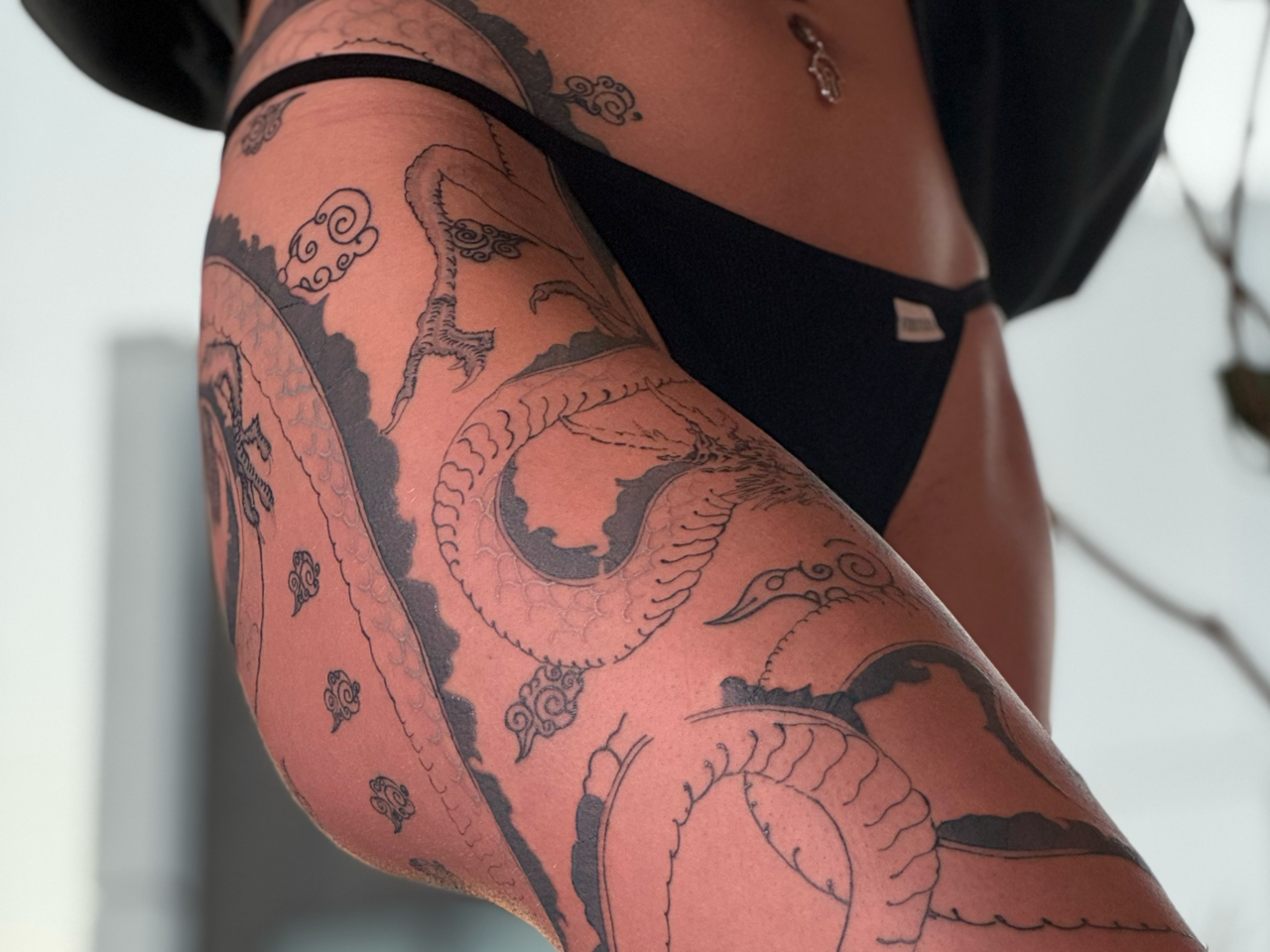 Fine-line dragon winding from hip to knee through stylized cloud bands